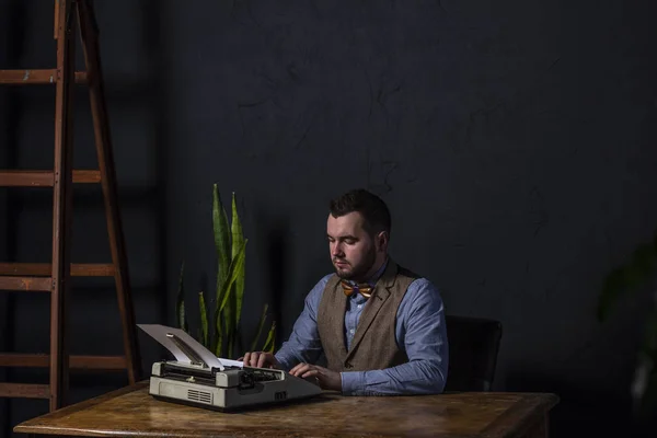 Bearded stylish writer typing on typewriter. Modern writer working on new book in office. Dark background. Space for text