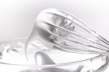 Metal whisk with whipped egg whites on white background clipart