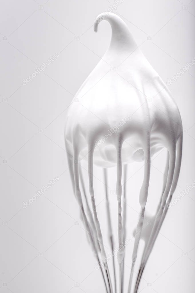 Metal whisk with whipped egg whites on white background