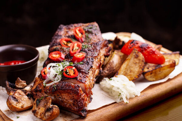 Delicious barbecued ribs seasoned with fresh herbs, cabbage salad, backed potato on an old rustic wooden chopping board