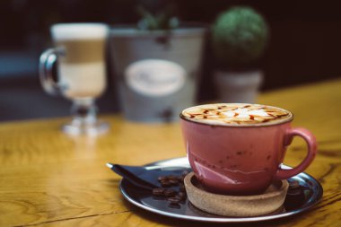Sıcak cappuccino köpüklü yüzeyi karamel dekorasyonu ile. Kahve çekirdekleri ile metal plaka üzerinde. Ahşap masa üzerinde arka plan ile bazı süs.