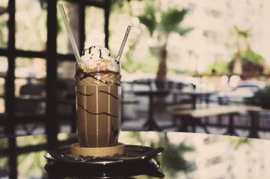 Krem buz kahve siyah yüzey üzerinde gülen yüz ile dekore edilmiştir. Kafede masada saman ile buzlu kahve.