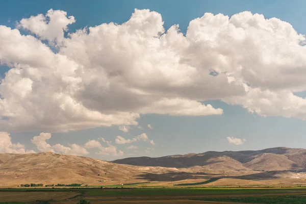 Big sky with big white clouds and hills beneath. Nature. Wide farm fields under the blue and cloudy sky in Turkey.