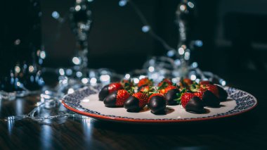 Çilek plaka üzerinde çikolata ile kaplı ve ışıkları ile dekore edilmiştir. Çilek hizmet vermeye hazır yakın görüntü.
