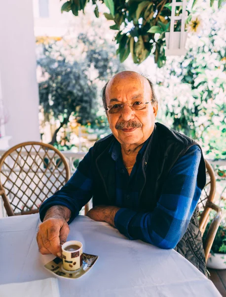 Elderly man sitting at the table and drinks turkish coffee. Stock Picture