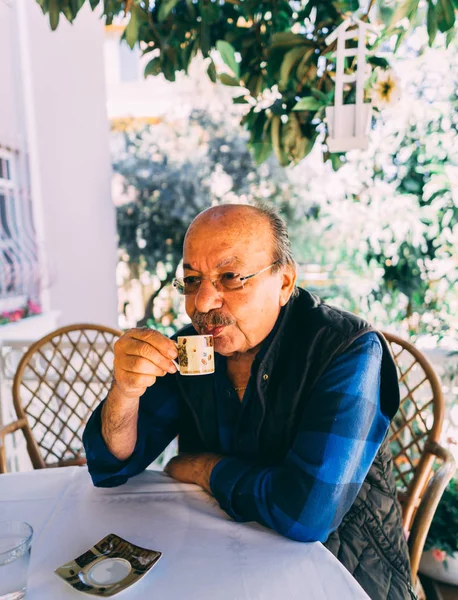 Elderly man sitting at the table and drinks turkish coffee. Royalty Free Stock Photos