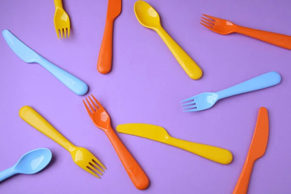 Många färgglada plasic gafflar, skedar och knivar på violett backgrou — Stockfoto