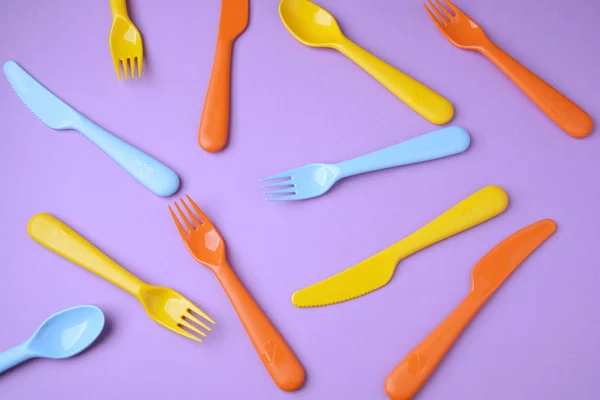 Many colorful plasic forks, spoons and knives on violet backgrou — Stock Photo, Image