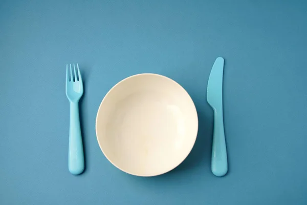 Синяя пластиковая посуда и белая тарелка на синем фоне. Концепция Лицензионные Стоковые Фото