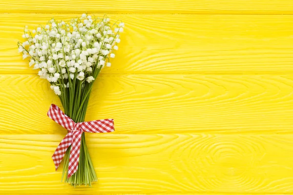 花束百合的山谷与红色丝带在黄色木桌从上面 母亲节 妇女节 情人节 生日背景 — 图库照片