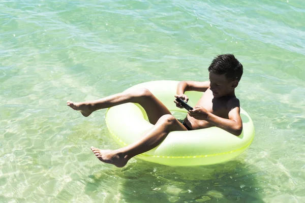 Boy swimming in inflatable ring with smart phone