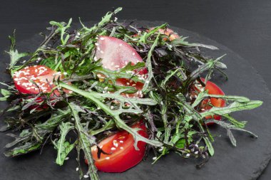 Domates, taze roka leavesand susam koyu ahşap arka plan üzerinde siyah plaka üzerinde taze yaz salatası.