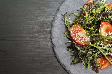 Domates, taze roka leavesand susam koyu ahşap arka plan üzerinde siyah plaka üzerinde taze yaz salatası.