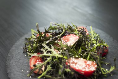 Roka, domates, susam ve zeytinyağı siyah bir plaka üzerinde otantik salatası. Seçilen odak yumuşak