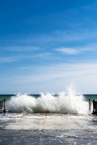 Sea water splashes at old pier on sunny day — Stock Photo, Image