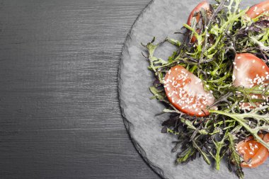 Roka, domates, susam ve zeytinyağı siyah bir plaka üzerinde otantik salatası. Seçilen odak yumuşak