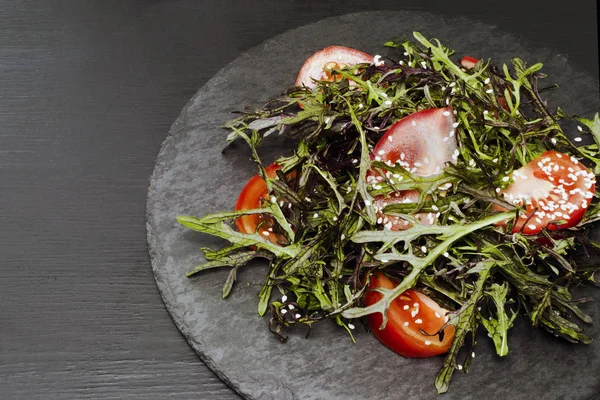 Roka, domates, susam ve zeytinyağı siyah bir plaka üzerinde otantik salatası. Seçilen odak yumuşak