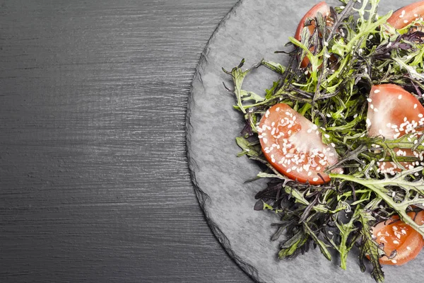 Roka, domates, susam ve zeytinyağı siyah bir plaka üzerinde otantik salatası. Seçilen odak yumuşak