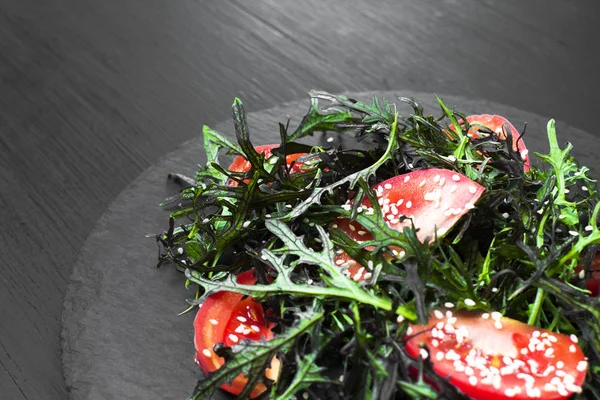 Roka, domates, susam ve zeytinyağı siyah bir plaka üzerinde otantik salatası. Seçilen odak yumuşak