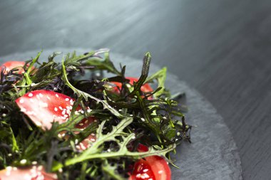 Roka, domates, susam ve zeytinyağı siyah bir plaka üzerinde otantik salatası. Seçilen odak yumuşak