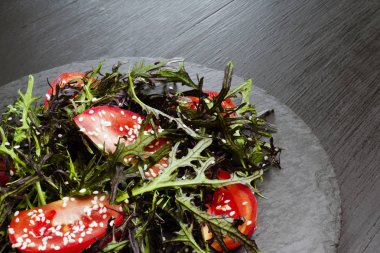 Roka, domates, susam ve zeytinyağı siyah bir plaka üzerinde otantik salatası. Seçilen odak yumuşak