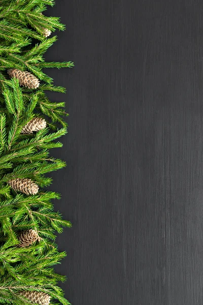 Christmas frame heart shaped made of natural fir branches and cones on black wooden background. Flat lay, top view — Stock Photo, Image