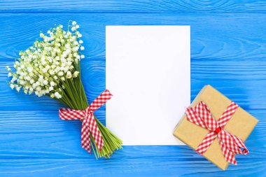 Mockup kokulu çiçekler lily vadi ve mavi ahşap masa, hediye kutusu üst görünüm sayfasında boş kağıt,