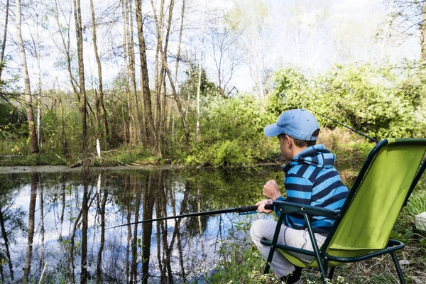 Niño triste y solitario con una caña de pescar se sienta en la orilla del lago — Foto de Stock