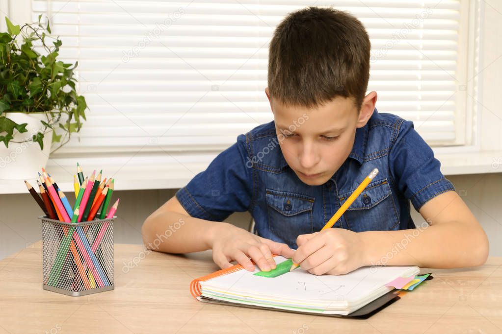 Boy draw in notebook. Child sitting at the desk home and doing his homework. School, children, education concept
