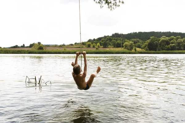 Nastoletni chłopiec skoki w rzece od wychylenia liny w słoneczny letni dzień. — Zdjęcie stockowe