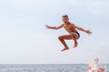 Havadan geniş bir nehirde suya atlayan mutlu 10 yıl çocuğu. Yaz tatili eğlence konsepti