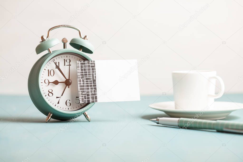 Mockup of retro style alarm clock with empty sticky note with copy space for text. Beginning of working day with coffee cup