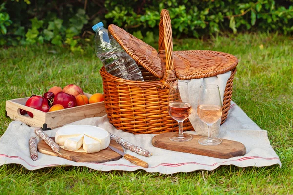 Picnic basket with different snacks on the green grass in the garden