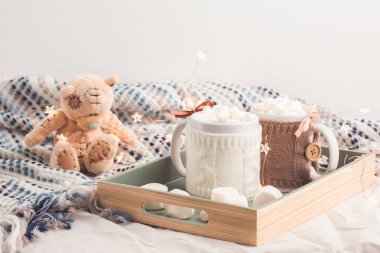 İki bardak sıcak çikolata şekerleme oyuncak ayı, Noel ışıkları yumuşak ekose zemin üzerine tepsiye.