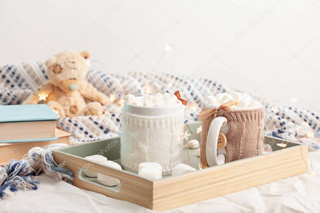 Still life of tray with two cups of hot chocolate with marshmallows on soft plaid background with teddy bear, Christmas lights and books.