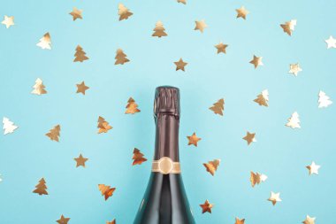 Şampanya şişesi mavi zemin üzerine konfeti ve Noel dekorasyonu ile yaratıcı fotoğraf