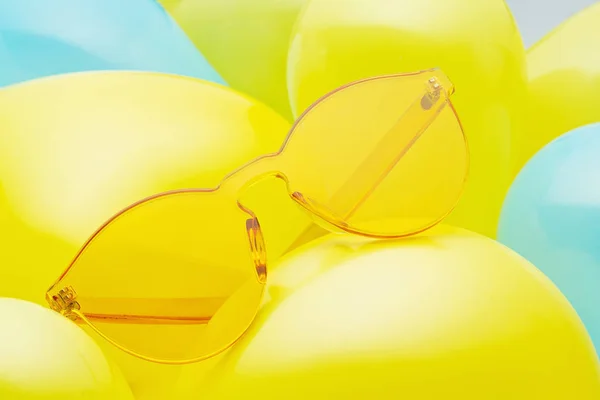 Top uitzicht van trendy zonnebrillen over de pastel achtergrond gemaakt met gele en blauwe ballonnen — Stockfoto
