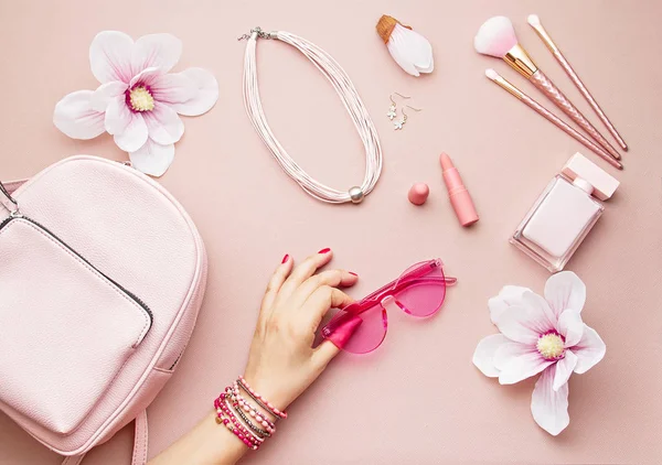 Flat lay with pink woman accessories  with backpack and woman hand holding the sunglasses. Summer fashion trends, shopping idea