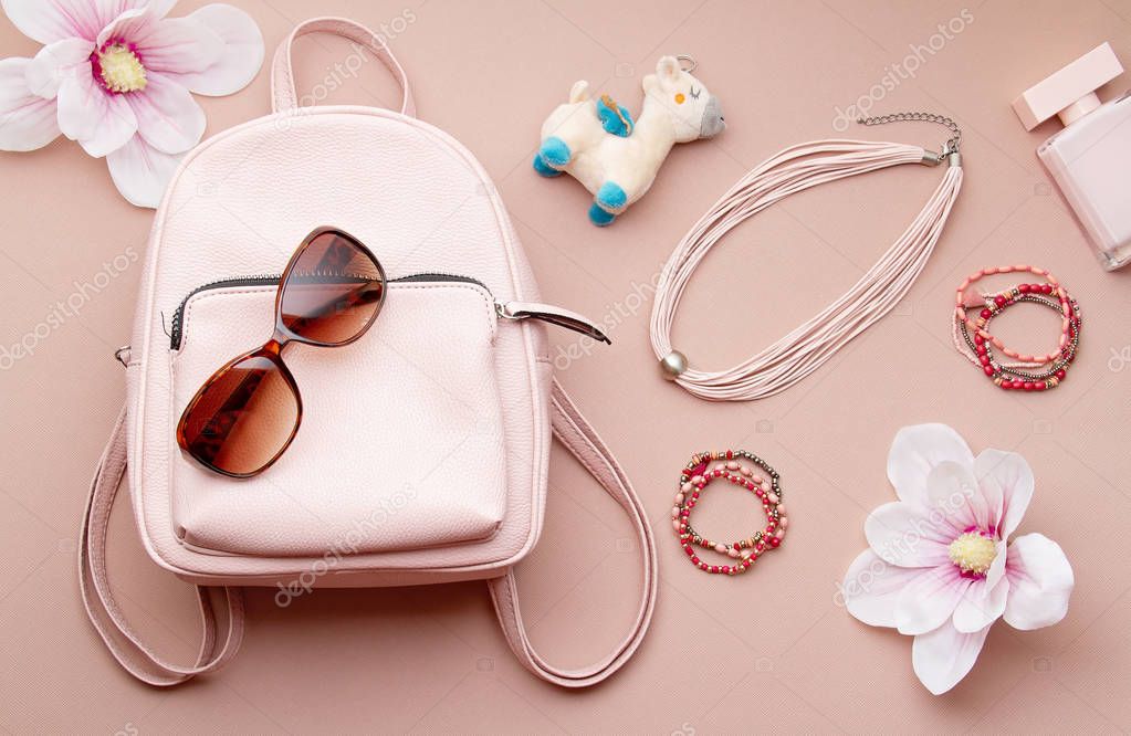 Flat lay with pink woman accessories  with backpack and woman hand holding the sunglasses. Summer fashion trends, shopping concept