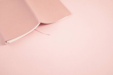 Pembe pastel arka plan üzerine açık bir defter. Çalışmak, okumak, rahatlamak. Monokrom minimal model, üst görünüm