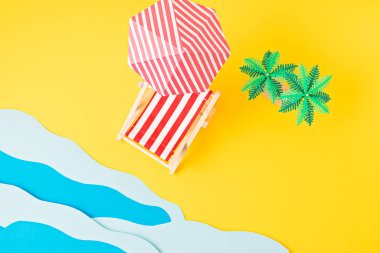 Güneş yatağı, oyuncak palmiye ağaçları, kağıt deniz dalgaları. Yaz tatilleri, sahil tatilleri, tatil konsepti.