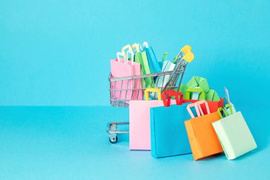 Kese kağıdıyla dolu bir alışveriş sepeti. Sesonal satış, online anlaşmalar, indirimler, promosyon, alışveriş bağımlılığı konsepti