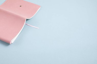 Mavi pastel arka plan üzerine pembe bir defter aç. Çalışmak, okumak, rahatlamak. Monokrom minimal model, üst görünüm
