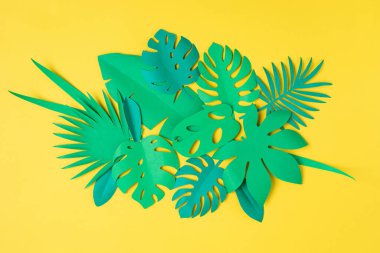 Sarı pastel arka plan üzerinde kağıt tropikal yapraklar. Yaz egzotik tatilleri, tebrik kartı maketleri. DIY projesi fikri. Üst görünüm düzlüğü