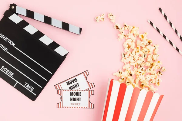 Movie clapperboard, tickets and popcorn over pink background. Movie night, home cinema, party invitation. Top view, copy space, mockup