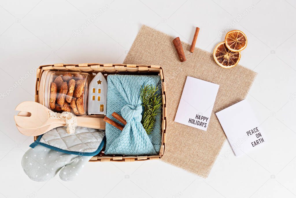 Preparing care package, sasonal gift box with kitchen utensils, furoshiki box and cookies. Personalized eco friendly basket for winter holidays. Top view, flat lay