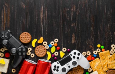 Tatlılar, bisküvi ve soda bidon arasında koyu ahşap arka plan üzerinde siyah beyaz modern gamepads. Düz yatıyordu kopya alanı oyun kavramını.