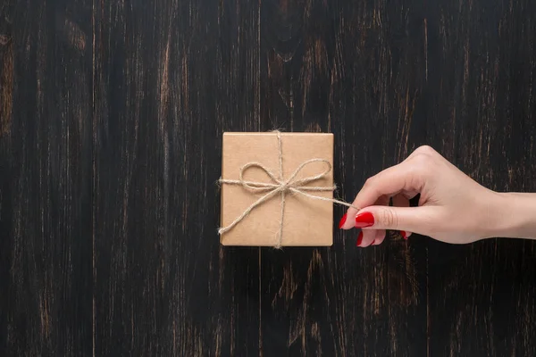 Hand of a young girl opening a gift box on a dark wooden background.