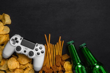 Modern beyaz gamepad cips, kraker ve siyah bir zemin üzerine bira şişesi arasında. Oyun kavramını.