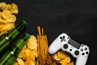 Modern beyaz gamepad cips, kraker ve siyah bir zemin üzerine bira şişesi arasında. Oyun kavramını.